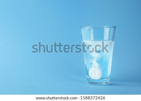 Glass of water with effervescent tablet on light blue background, space for text