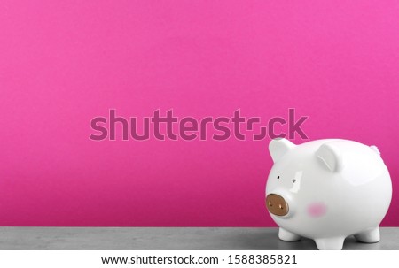 White piggy bank on light grey table against pink background. Space for text