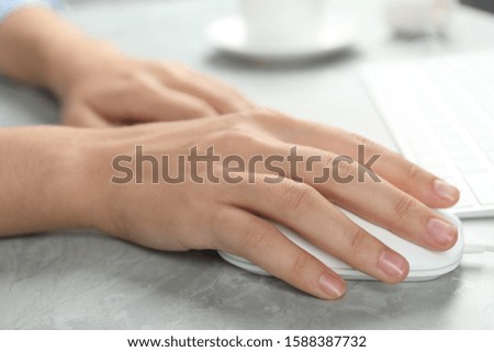 Woman using wired computer mouse at light grey marble table, closeup