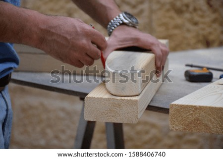 Man doing woodwork carpentry work, measuring piece of pine wood (wood block) with a pencil before cutting it into rounded shape, making a furniture. woodworking carpenter workplace, carpenter hands. Royalty-Free Stock Photo #1588406740