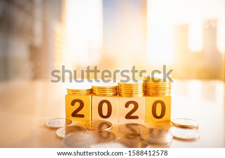 Wooden number 2020 with stack of coins on blurred city scape and copy space for text using as background business investment, new year concept.
