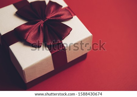 Red Christmas background with gift box.Winter holiday presents packed in decorative paper package decorated with red ribbon on top.Beautiful handmade present for New Year celebration party in December