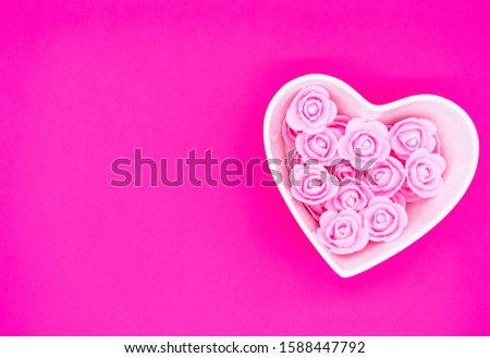 Roses laid out in the shape of a heart on a bright pink backdrop. Valentine's day, International Women's Day background. Empty copy space for your text.