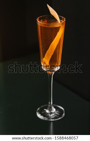 Sparkling orange alcoholic drink with orange zest in a long glass on a dark background.