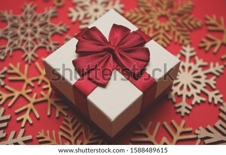 White Christmas gift box with red ribbon on wooden snowflakes toys in close up.Winter holidays decorations and presents