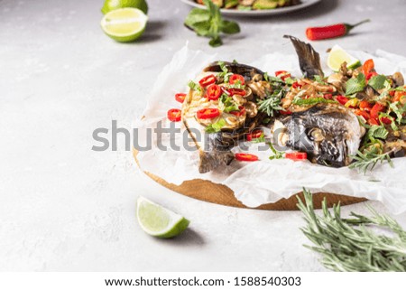Baked dorado or sea bream fish with lime, chilly, herbs and vegetables, light grey stone background. Selective focus. Keto diet. Comfort food.