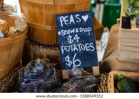 A closeup view of a traditional price sign advertising organic snow and snap peas and potatoes on a market stand during a local agricultural fair