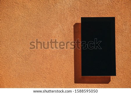 Empty black plate with copy space on orange wall background in minimal style.