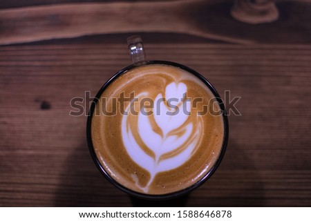 Coffee art concept. A cup of coffee with leaf pattern in a glass cup on wooden background.