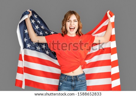 Young woman wearing sports clothes studio standing isolated on grey background holding american flag supporting favorite team on championship shouting happy