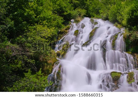 Wild, large waterfall, long exposure along green thickets. White water drop down