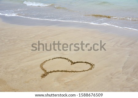 A heart written on the sand with wave crashing on the background 