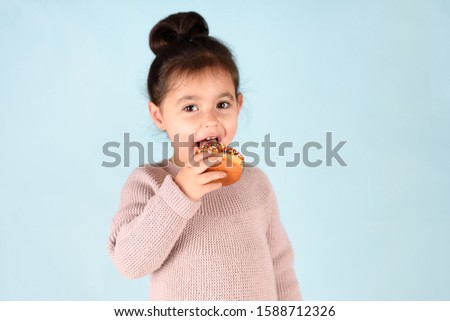 Little happy cute girl eating donut on blue background.