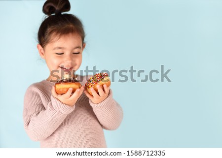 Little happy cute girl eating donuts on blue background. Child having fun with donut.