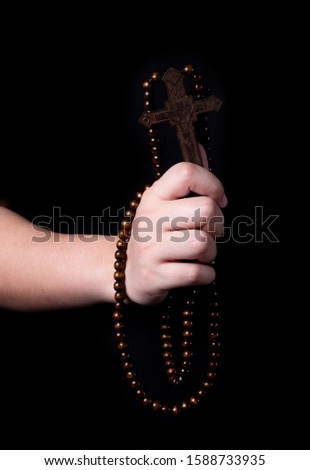 closed up hand holding wooden carved cross and rosary beads on black background.