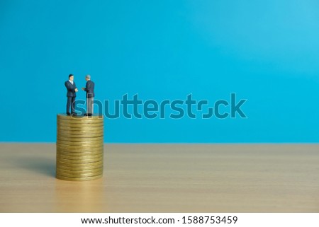 Miniature business concept - two businessman make an handshake for partnership agreement handshake with coin stack