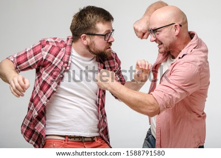 Two friends in glasses had a fight. They violently fight on their fists, angrily look at each other and grin their teeth.