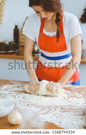 Young brunette woman cooking pizza or handmade pasta in the kitchen. Housewife preparing dough on wooden table. Dieting, food and health concept