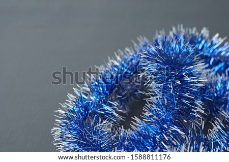 Scattered shiny festive tinsel of blue color on dark concrete desk. Space for text