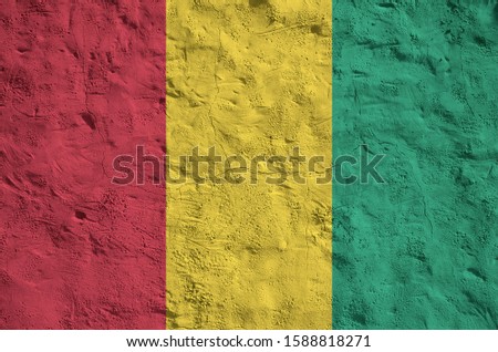 Guinea flag depicted in bright paint colors on old relief plastering wall. Textured banner on rough background