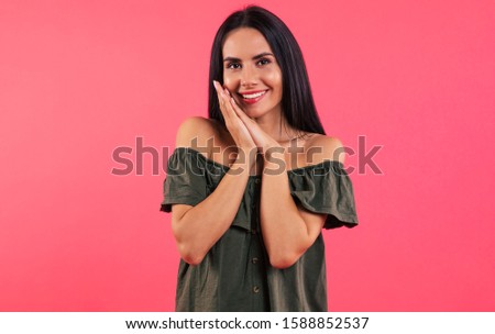 Lovely look. Close-up photo of a cute girl in a dark green dress, who is looking in the camera and smiling broadly, pressing her palms together near her chin.