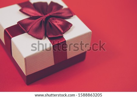 Christmas present box with ribbon on red background.Decorated white present package for Happy New Year celebration.Empty clear space for text.Winter holiday celebration party poster