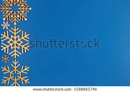 Blue Christmas background in flat lay style.Wooden snowflakes shot from above on paper backdrop.Postcard template with empty space for invitation text.Winter holiday back ground with rustic toys