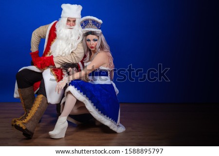 Positive Santa Claus in a red coat and Snow Maiden in a blue suit posing on a red background