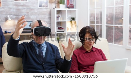 Elderly couple using modern technology to watch movies. Senior with virtual reality goggles. Old lady with laptop.