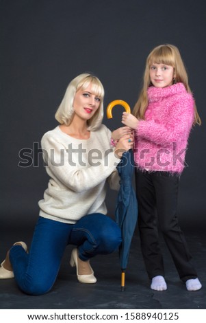 Mother and daughter (woman and girl) hold on to a large umbrella.