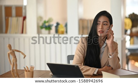 Young woman calling on cell phone in creative work desk.