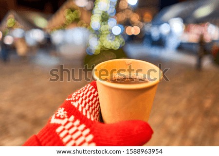 Hand holding a cup of mulled wine with blurred background of winter wonderland, a Christmas Market in European small city