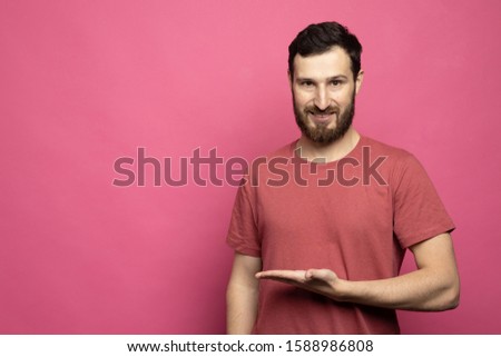 Casual dressed young bearded man in pink t-shirt pointing isolated on pink background