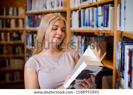 Blond student girl with book in library. Diligent student reading a book, preparing for classes, eager to study
