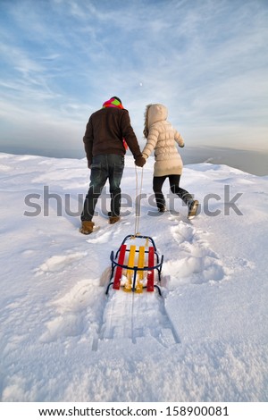Young couple pulling up a sled at snow