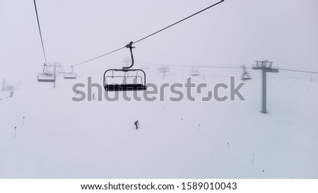 Ski chairlift moving in a foggy day and snowy mountains. Ski resort concept