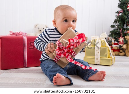 First Christmas: barefoot baby unwrapping a red present
