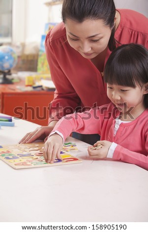 Teacher helping young girl with cut-out alphabet letters