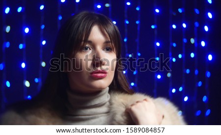 young girl posing in Arctic Fox fur coat beige on a background of blue garland.