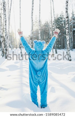 A vertical shot of a person in a fluffy blue costume standing with hands up in a forest in winter - back to childhood concept