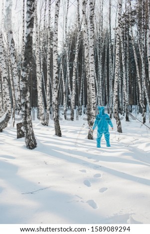 A vertical shot of a person in a blue fluffy costume walking in the snow in a forest like a bear