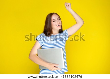 Young woman holding laptop computer on yellow background