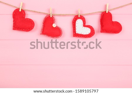 Fabric hearts with clothespins hanging on pink wooden background