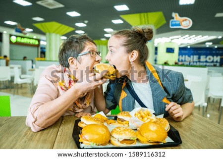 elderly woman, granny with a woman, daughter eagerly eat a hamburger
