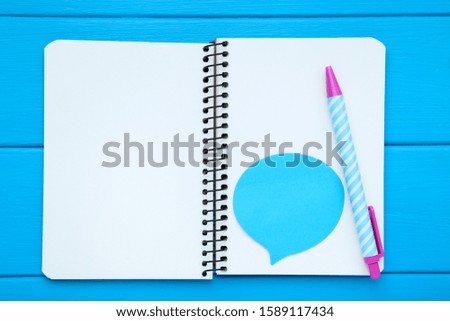 Blank notepad with pen and paper speech bubble on blue wooden table