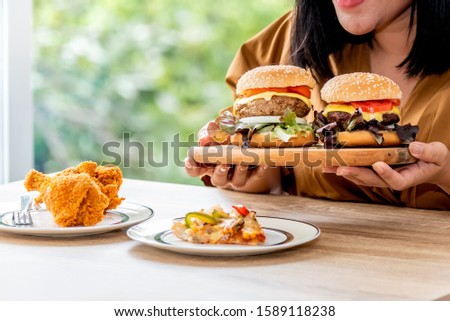 Fat women Happy to eating with the food she prepared Which has fried chicken, hamburger and pizza, This picture focuses on hamburger, to Cholesterol and excess fat concept.