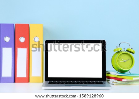 Laptop computer with folders, notepads and alarm clock on blue background