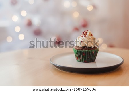 Green christmas cupcake with colorful sprinkles in pink cup on wooden background with garland lights bokeh