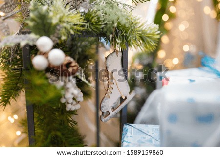 Christmas tree branch with cone and wooden skates toy hanging on it. Unfocused background with golden bokeh. Winter holidays, magic, miracle, Happy New Year. Place for text.