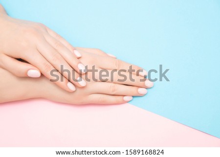 Beautiful female hands with stylish nail manicure gel polish on pink and blue background, top view. Skin care concept.